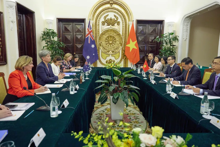 Two groups of people sitting at tables facing each other with the Australian and Chinese flags in the background