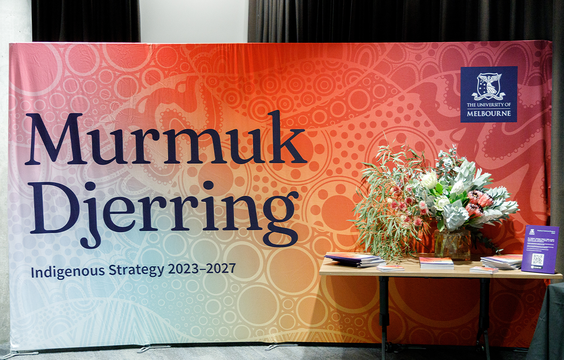 Large banner with Indigenous artwork background behind a small table with flowers on it