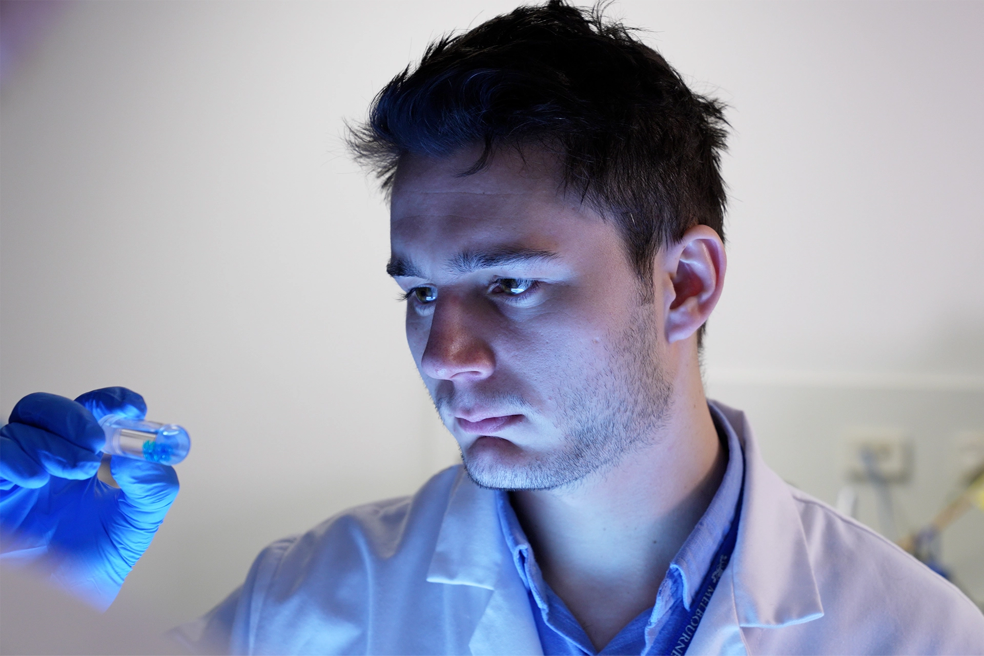 Man wearing white lab coat looking into glass lab vial