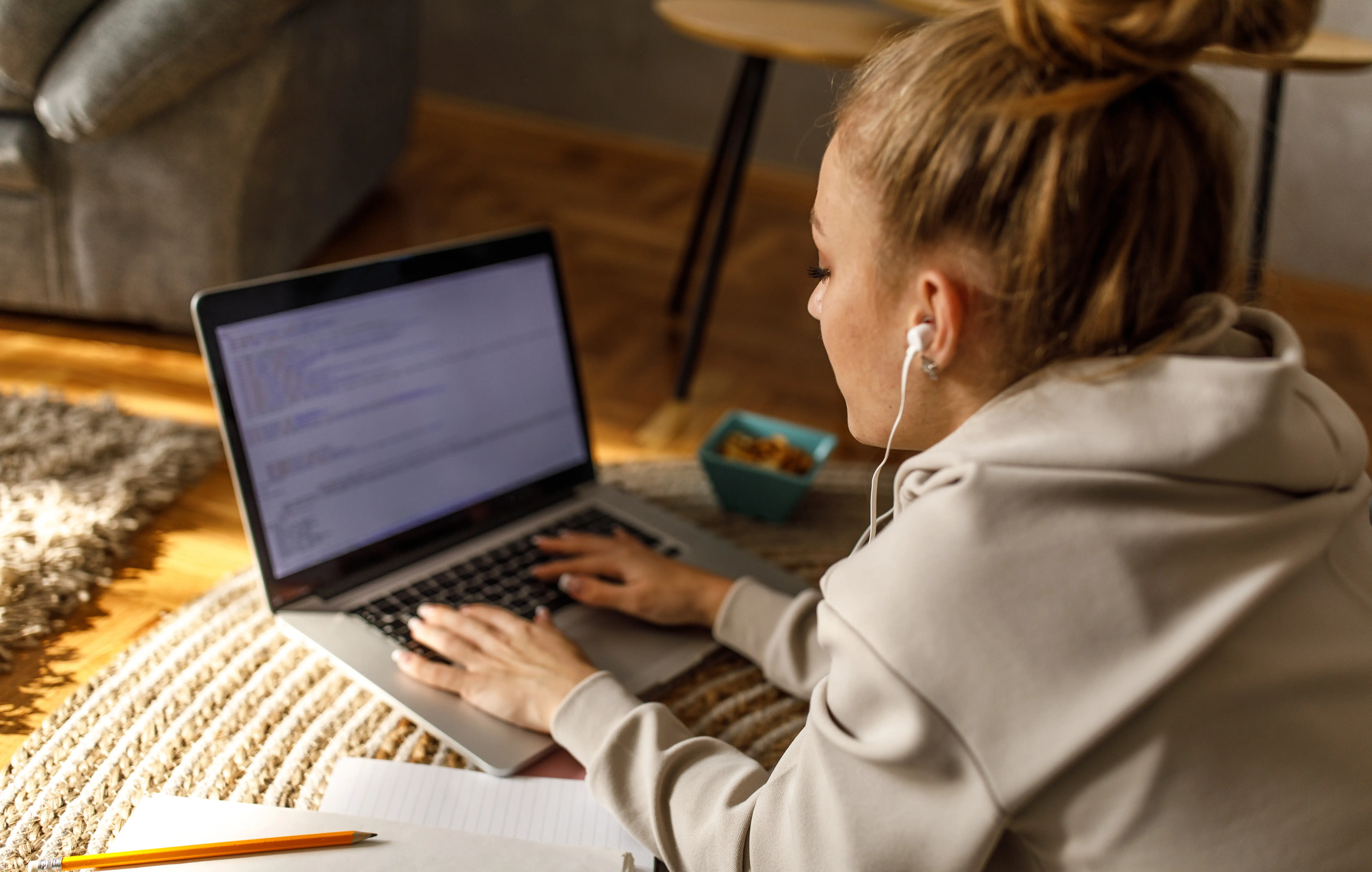 A young woman typing an essay on a laptop while wearing headphones and listening to music.