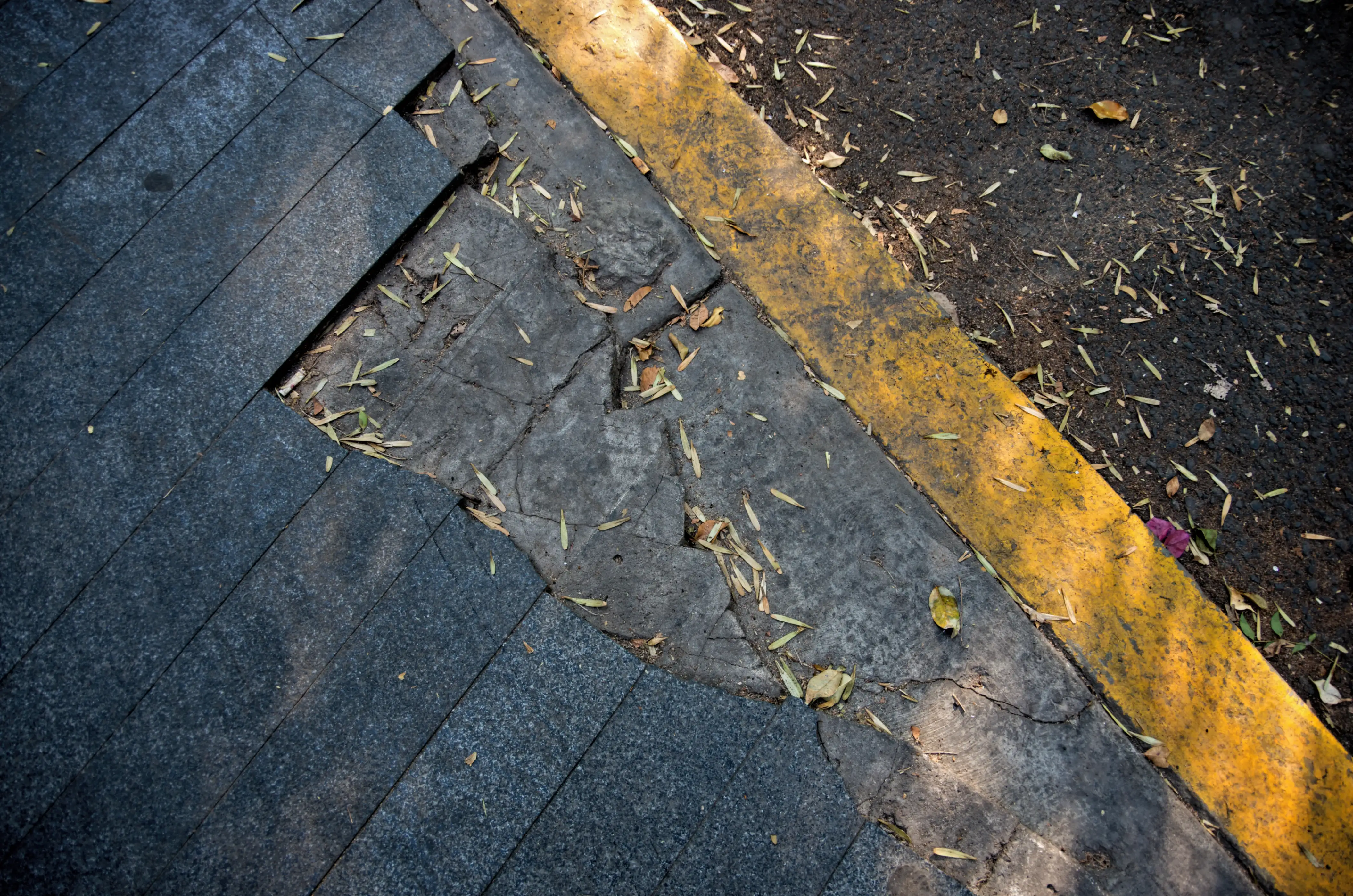 Broken stone tiles on a kerbside footpath