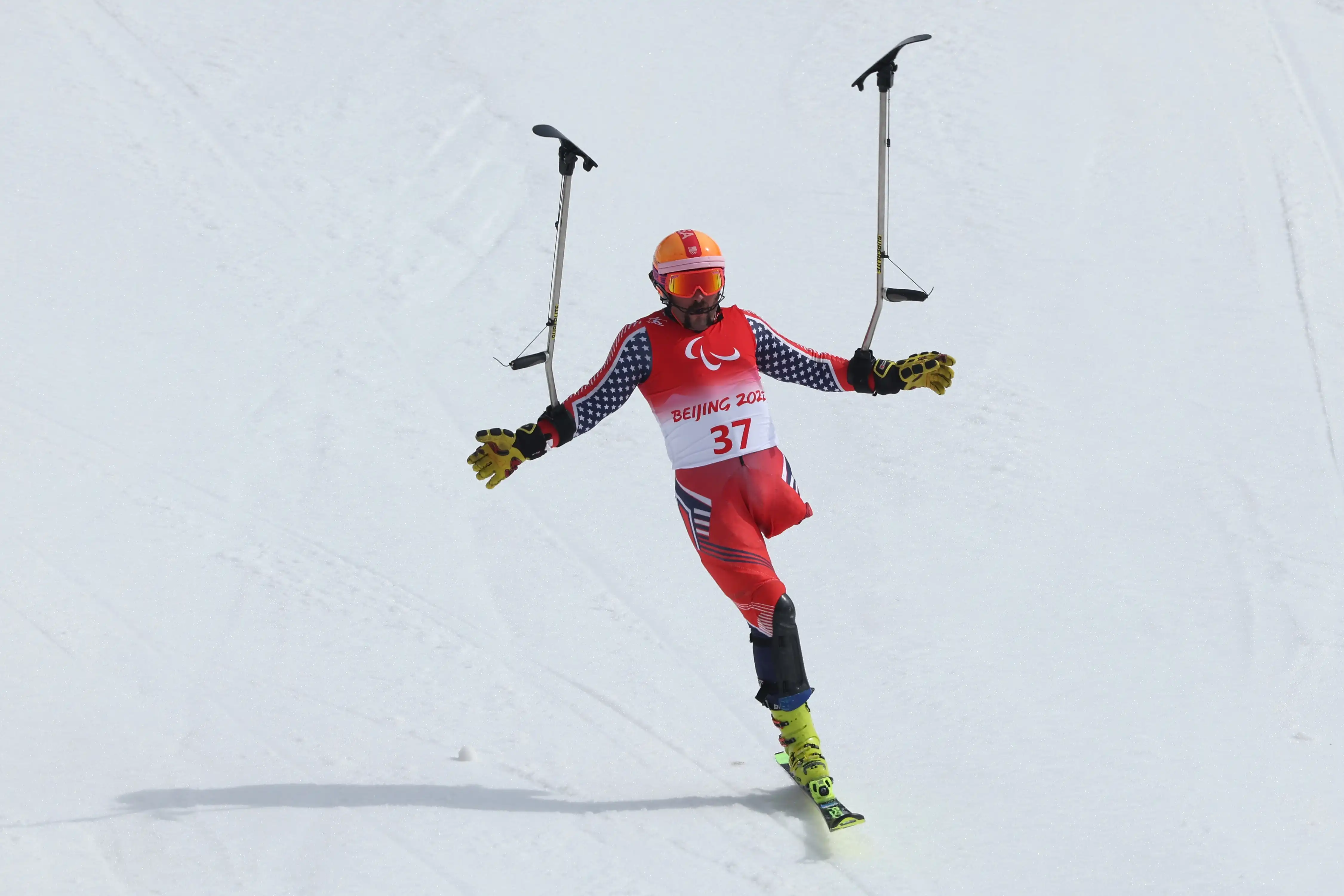 An amputee Paralympian skiing on one leg, holding his outriggers in the air as he comes down a hill