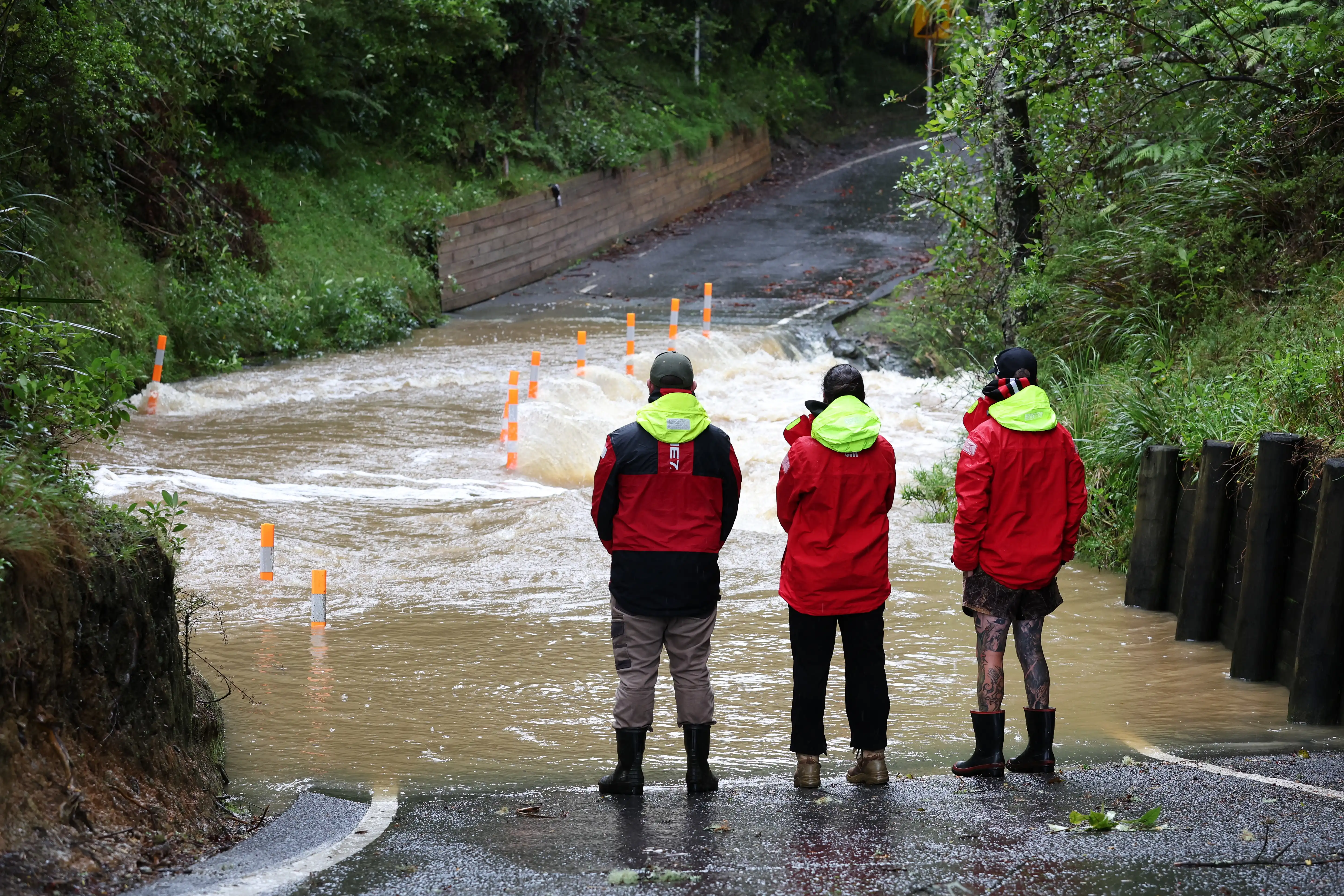 Three men stand in front of a winding road that has been flooded