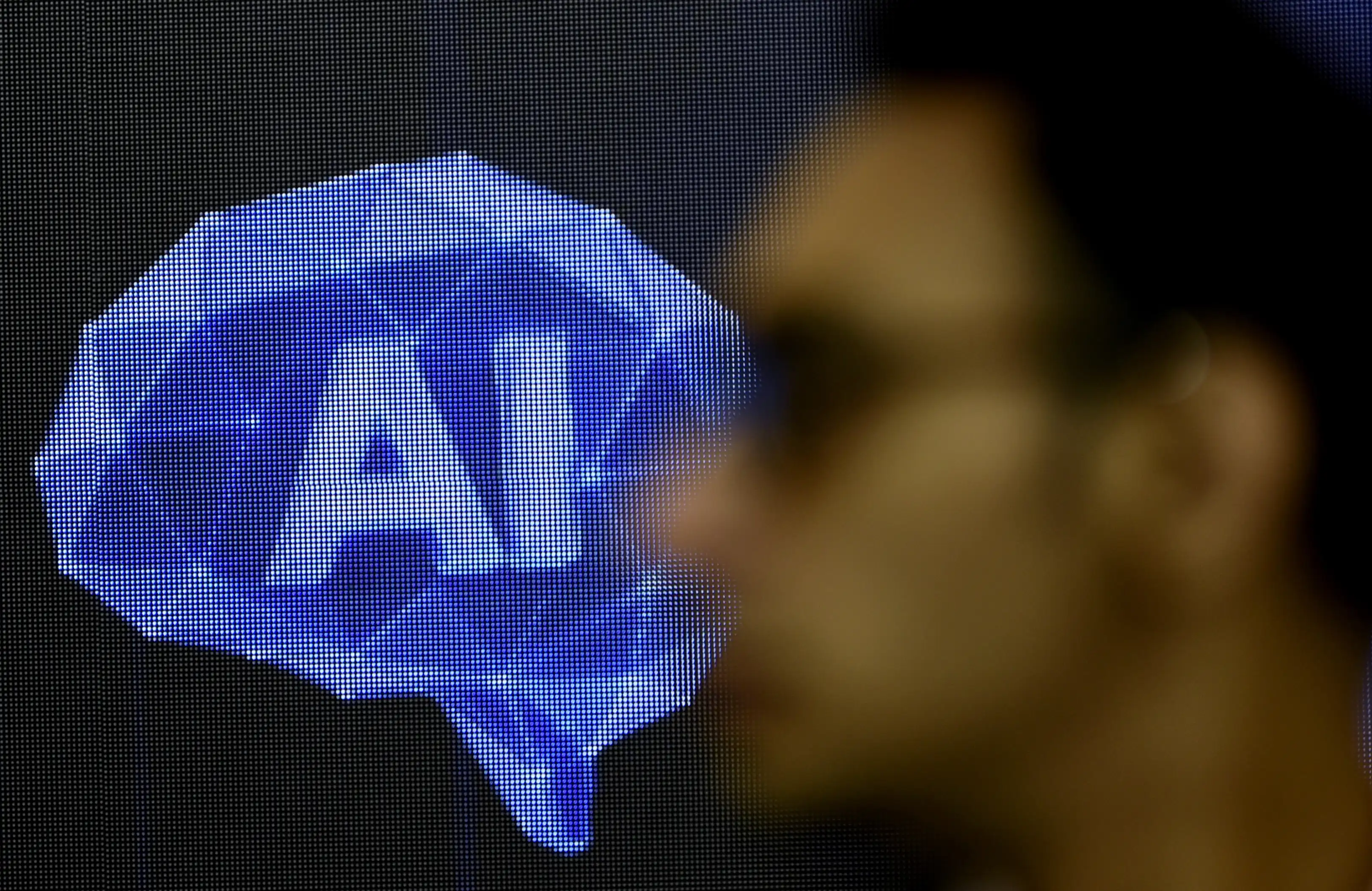 A blurred out face of a man standing in front of an AI symbol displayed on a large screen