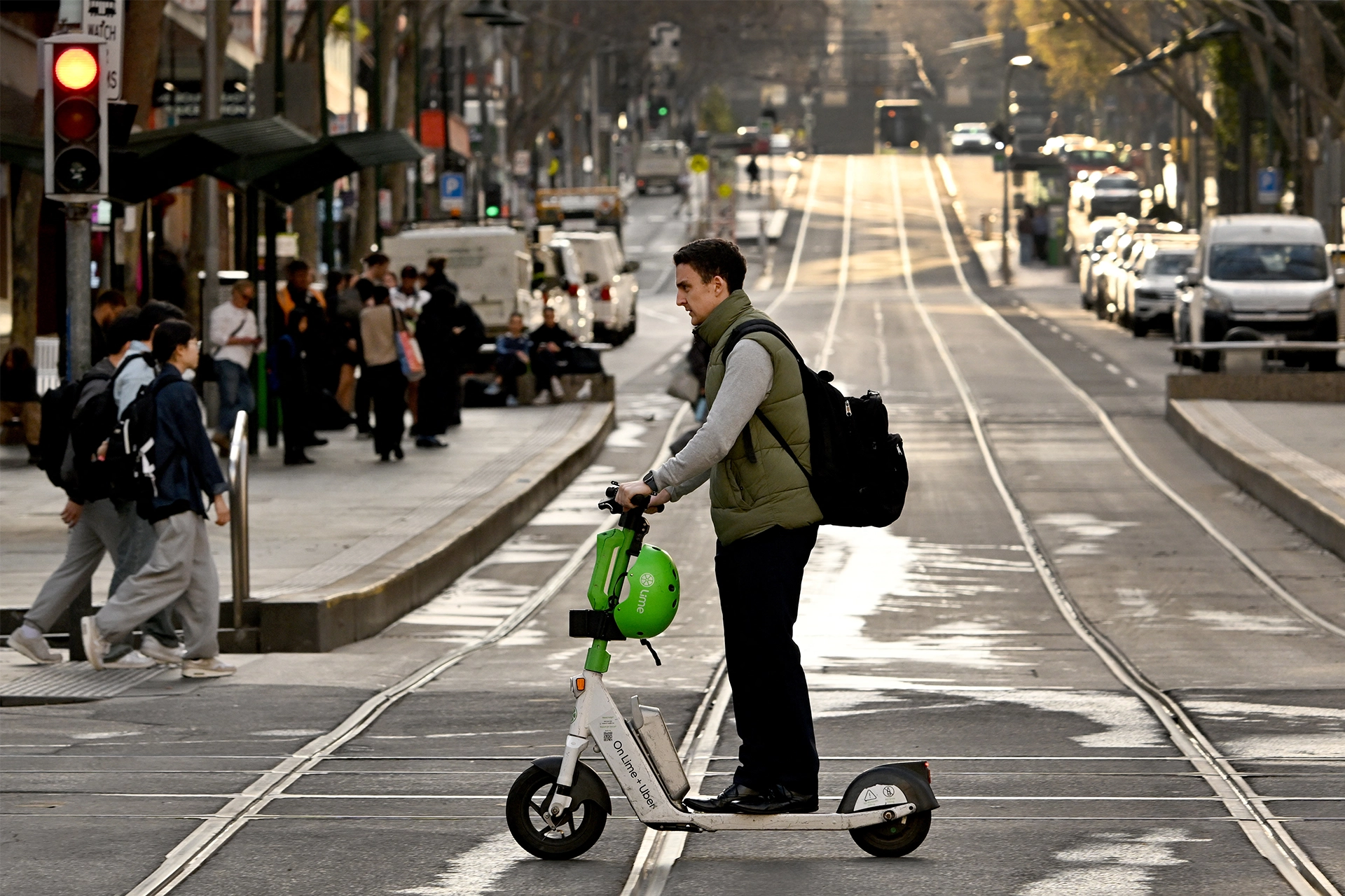 Man riding a shared e-scooter across tram tracks in Melbourne CBD, not wearing a helmet