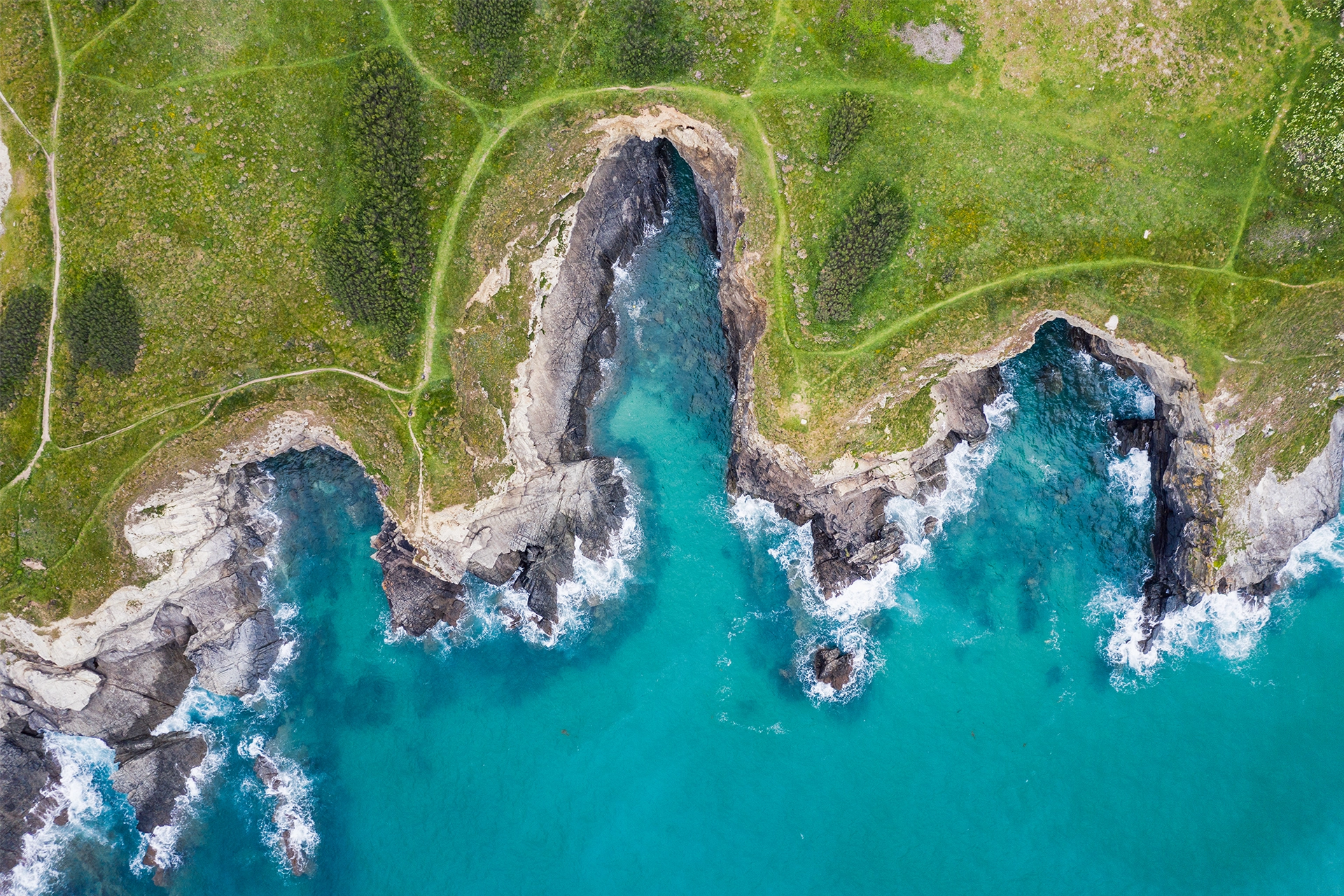 Aerial shot of UK coastline, showing green fields, jagged cliffs and bright blue ocean