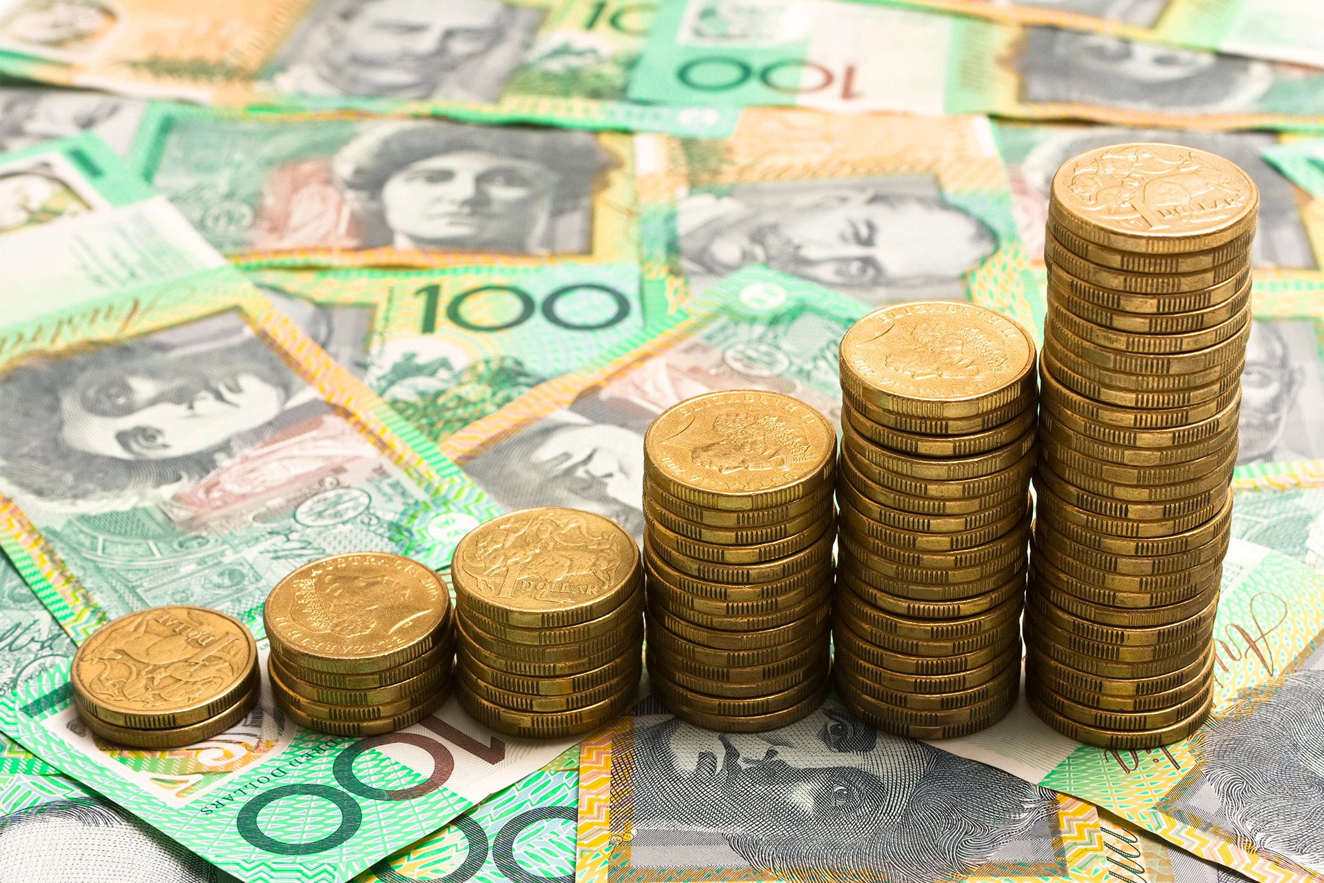 Australian $100 notes laid out on a surface with stacks of $1 gold coins sitting on top