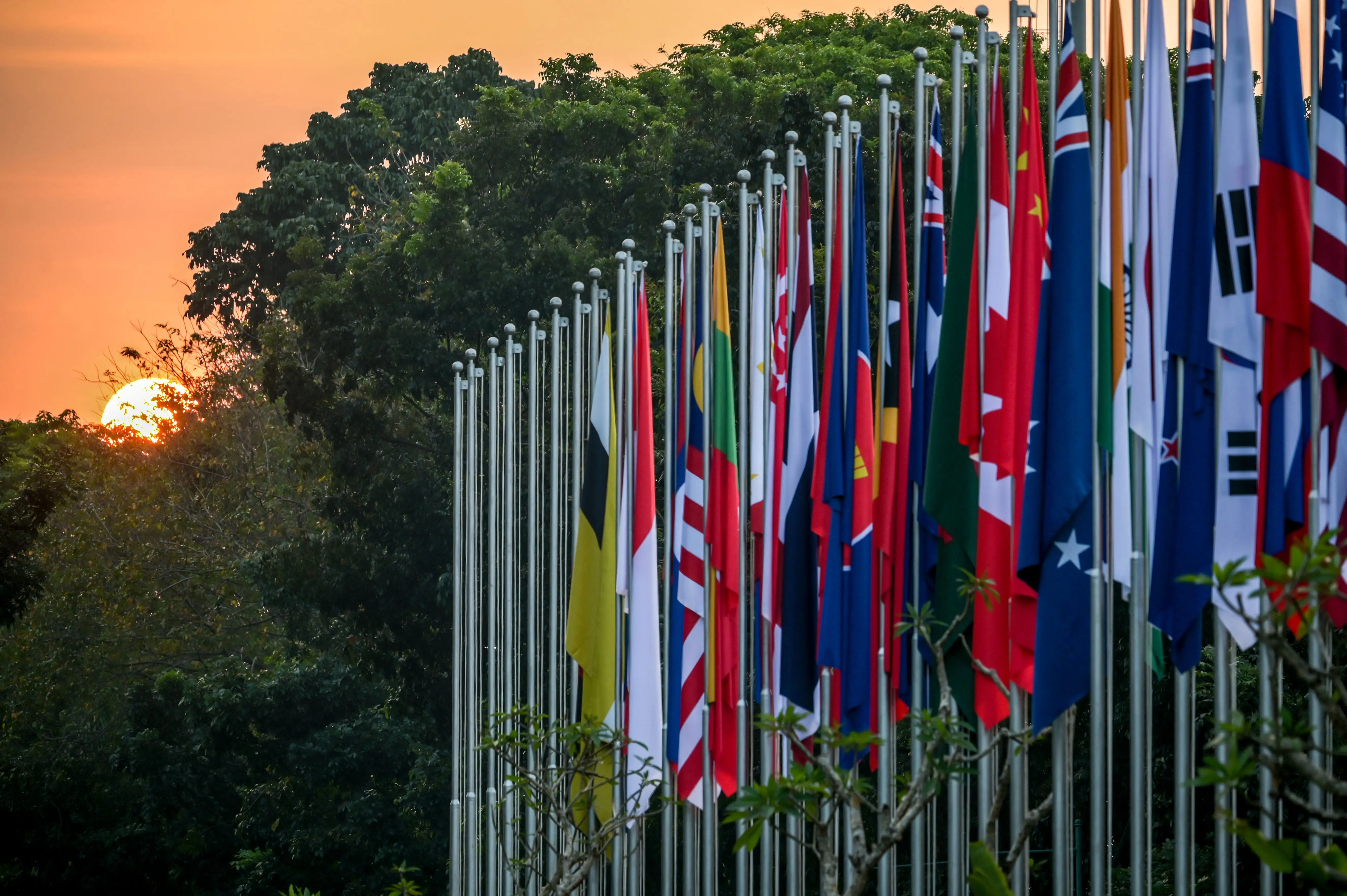 The sun sets behind tree behind Association of Southeast Asian Nations (ASEAN) flags 