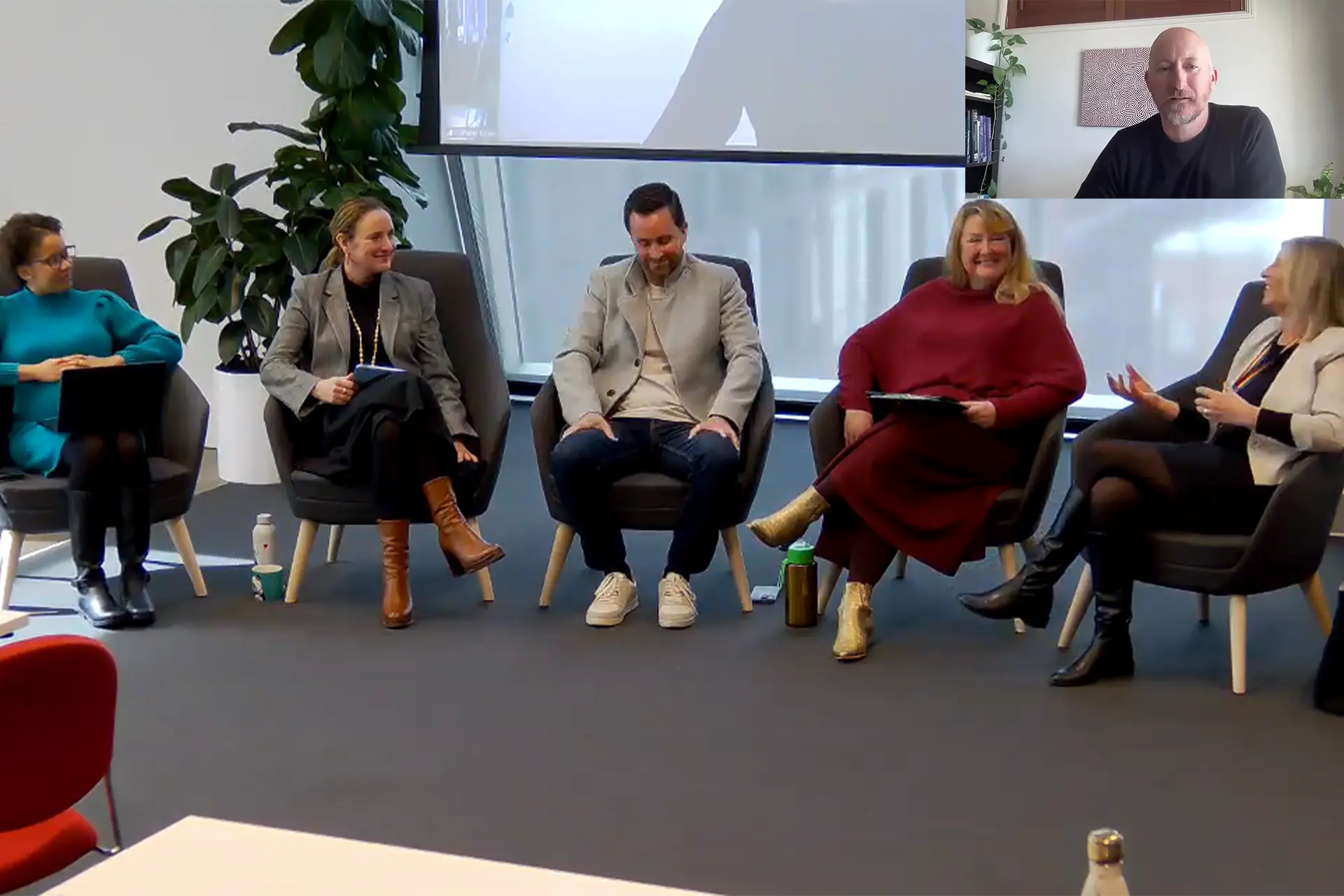 Panel of five people on chairs with another person joining the discussion from a screen