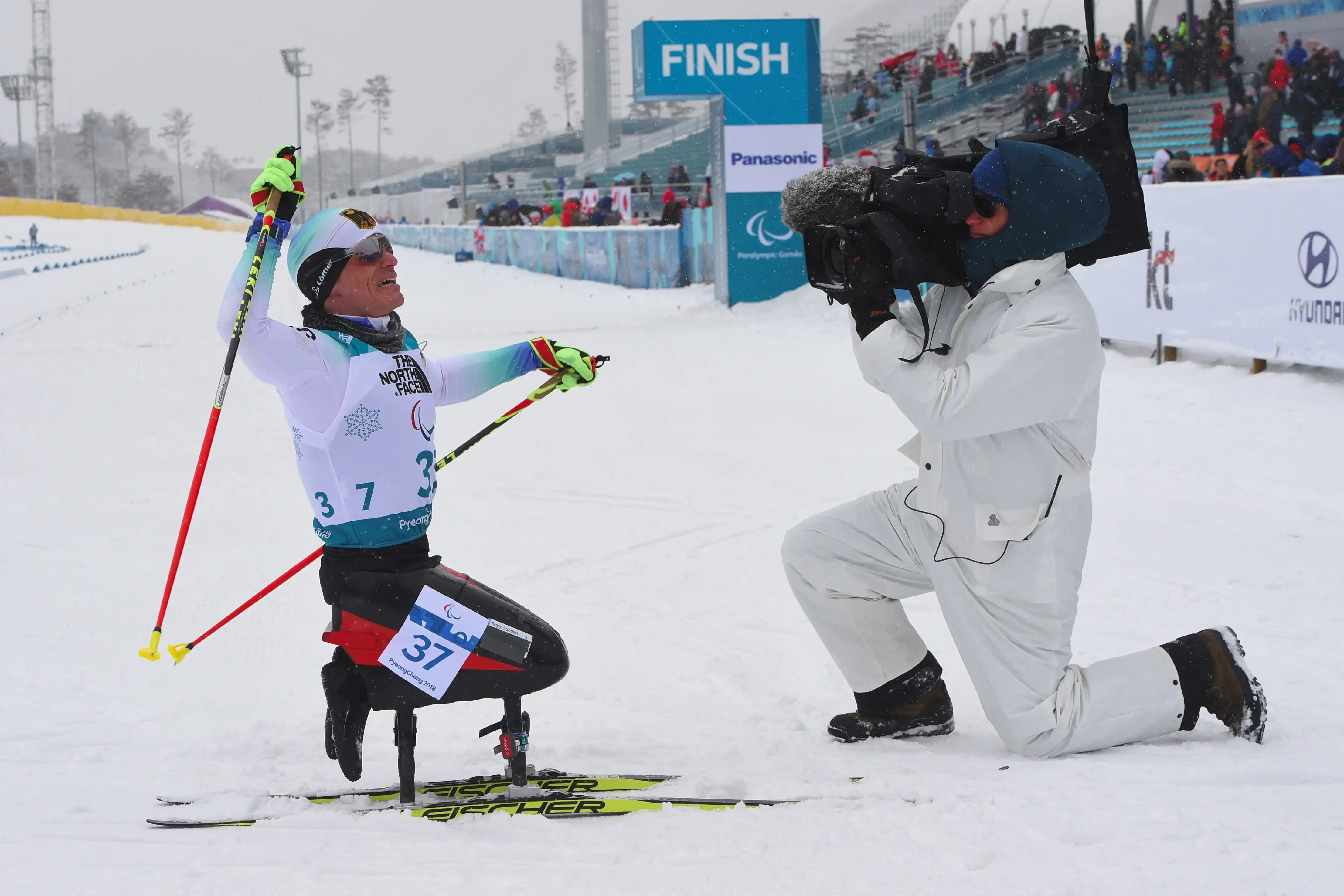 A cameraman films a man in sitting skis following his victory in a Winter Paralympics event in 2018
