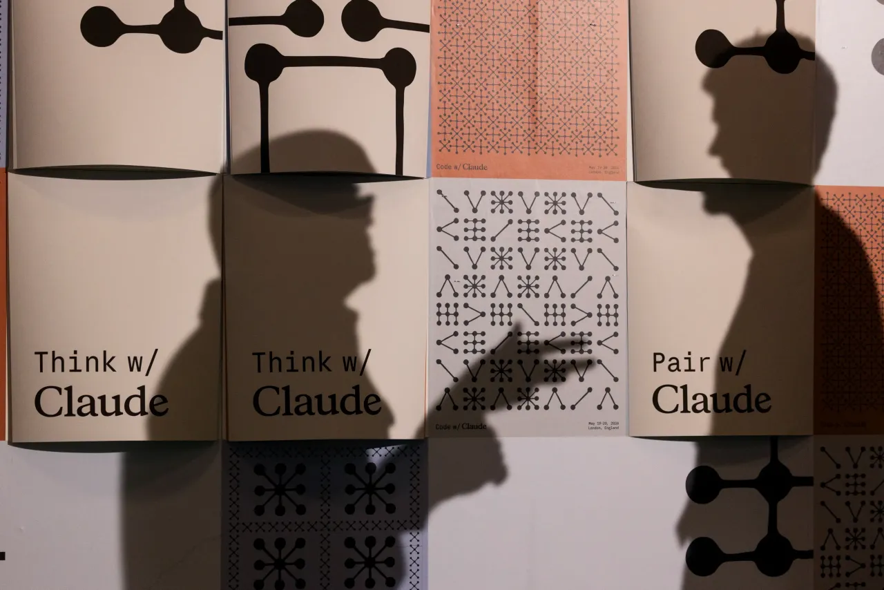 The silhouetted shadows of two people talking in front of posters for Anthropic's Claude