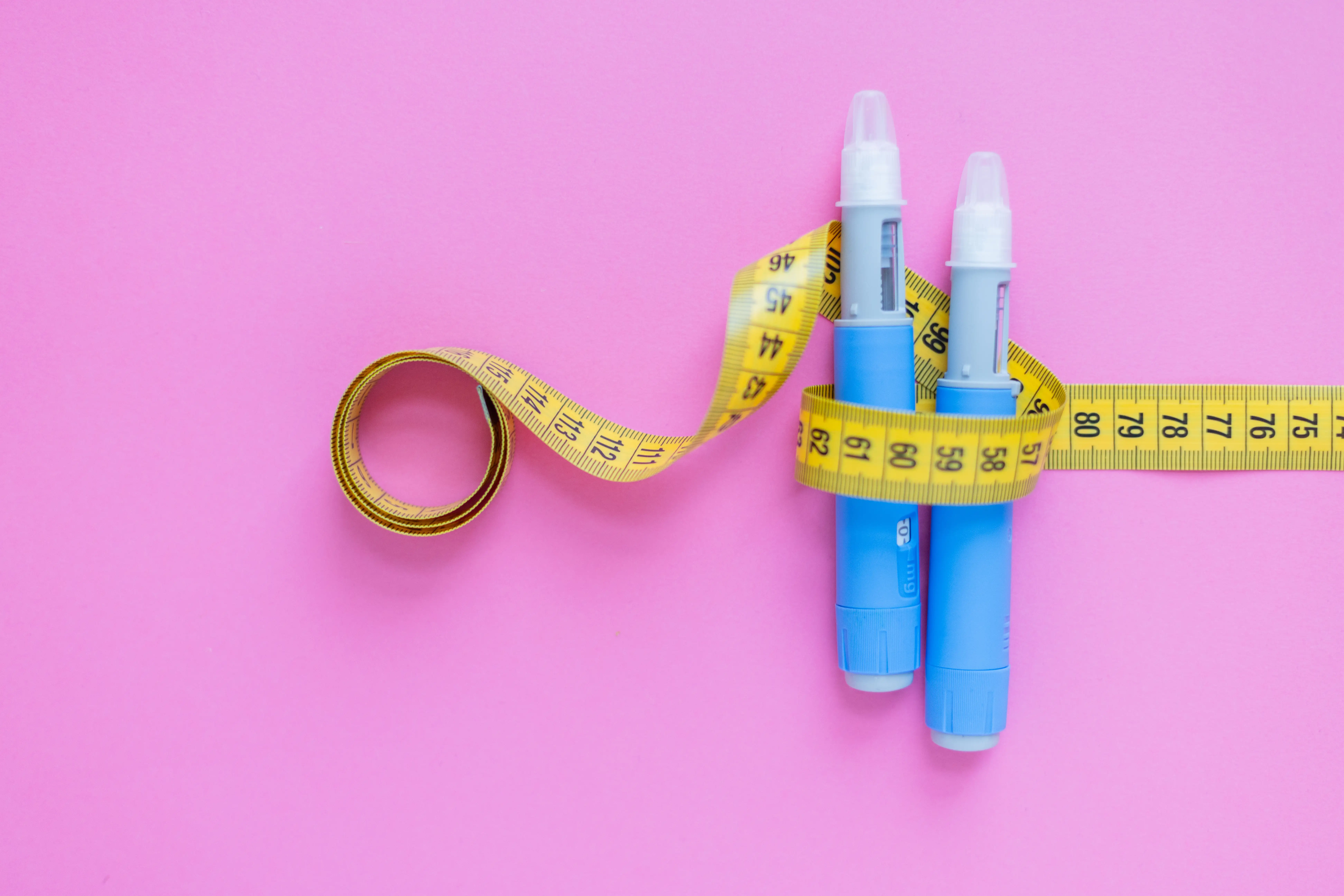 Diabetes and weight loss medication wrapped in yellow tape measure on a pink background 