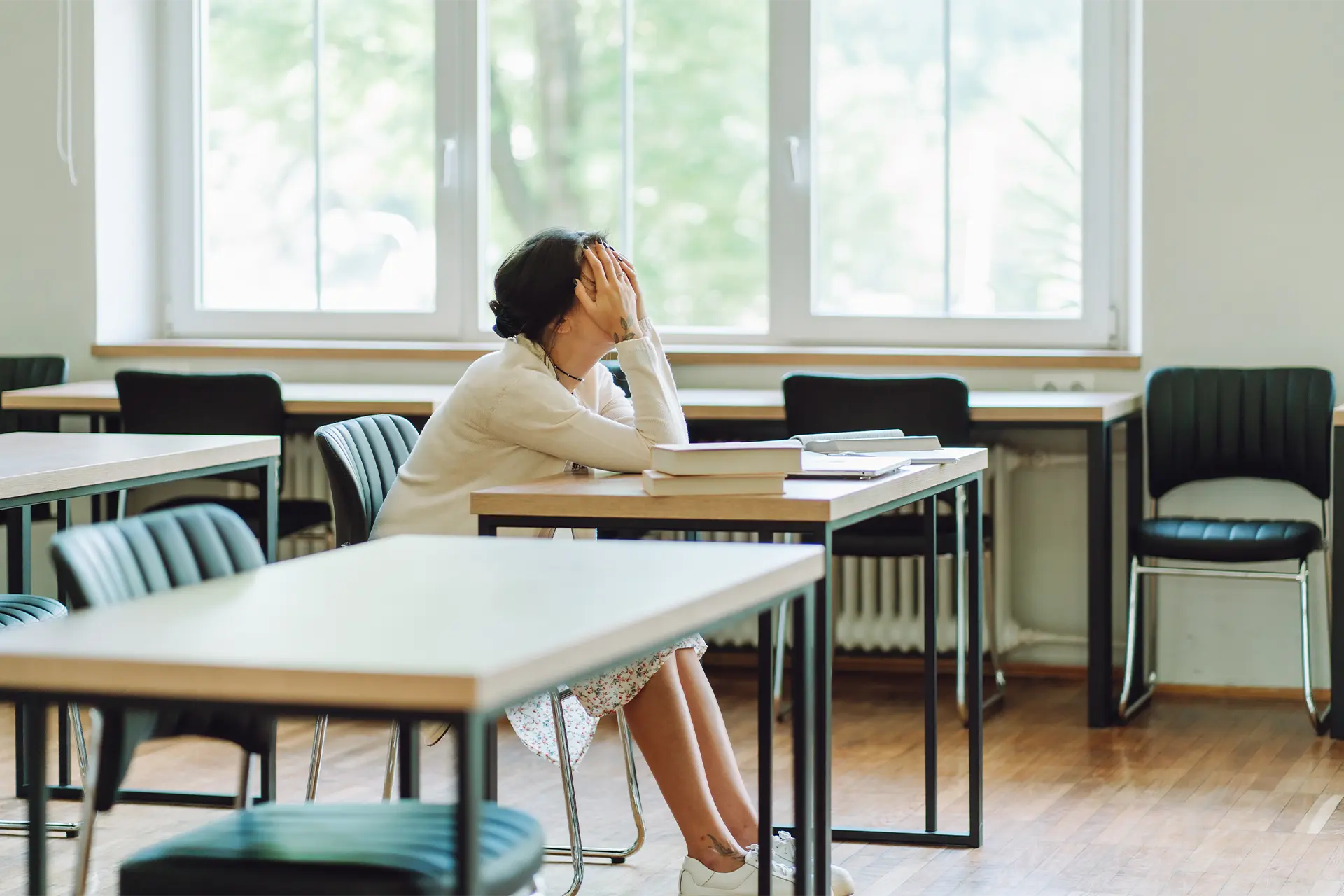 A teacher sitting at a school desk with her head in her hands
