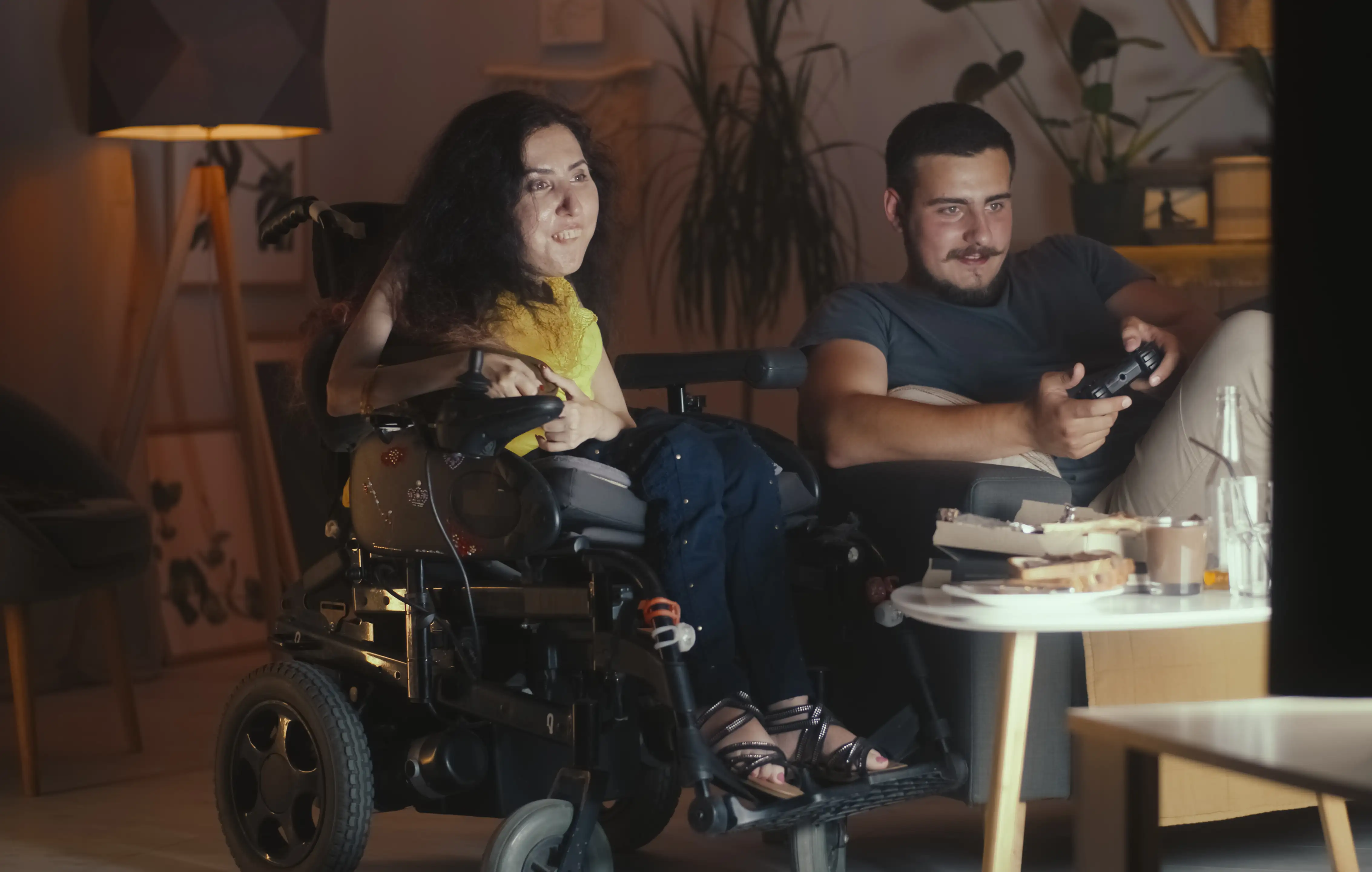 Man playing in video game console on TV using gamepad and woman with a physical disability sitting in a wheelchair at watching it