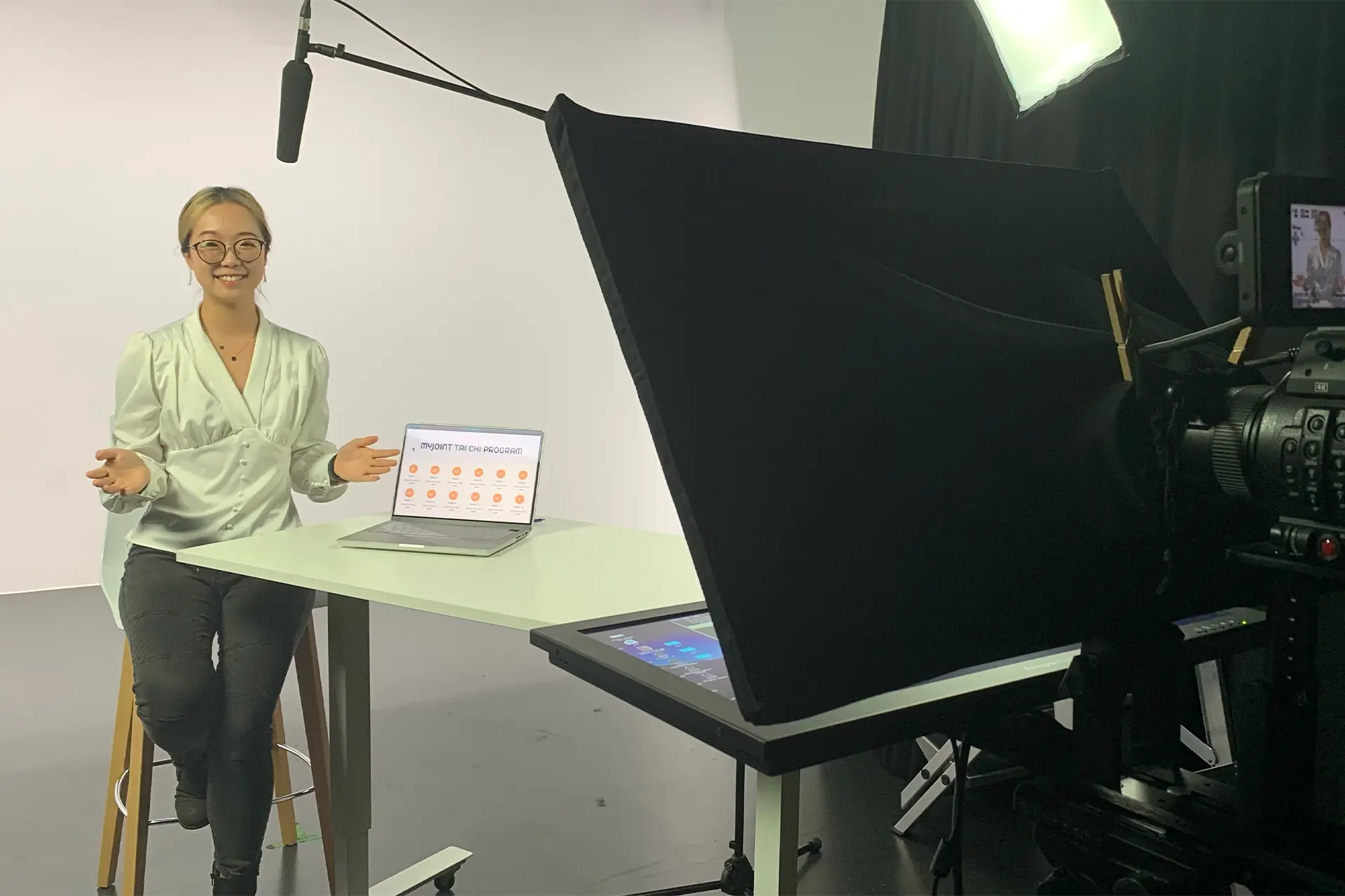 A woman sitting at a desk in front of a camera in a recording studio