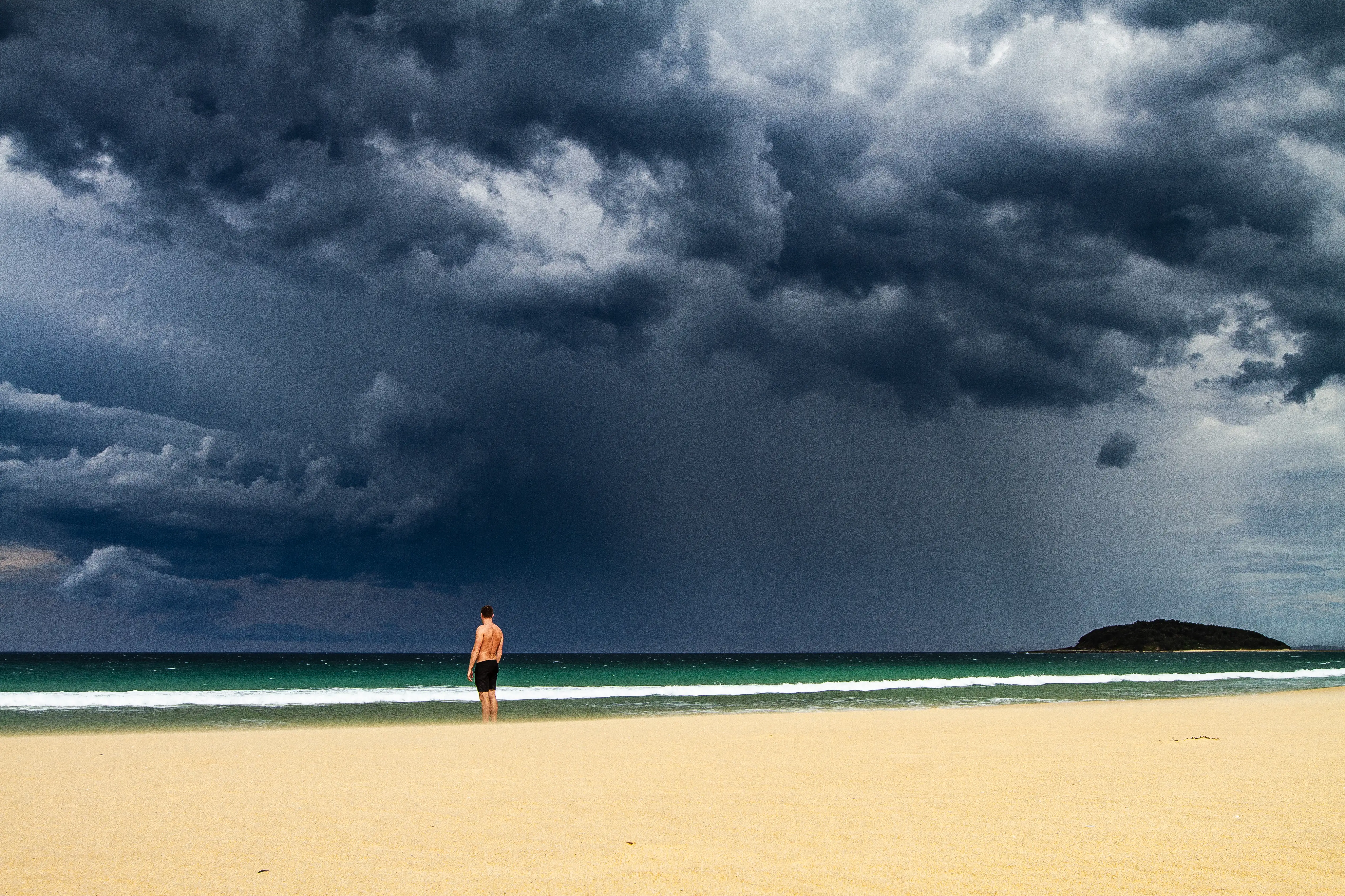Dark storm clouds over a sunny beach with a single swimmer