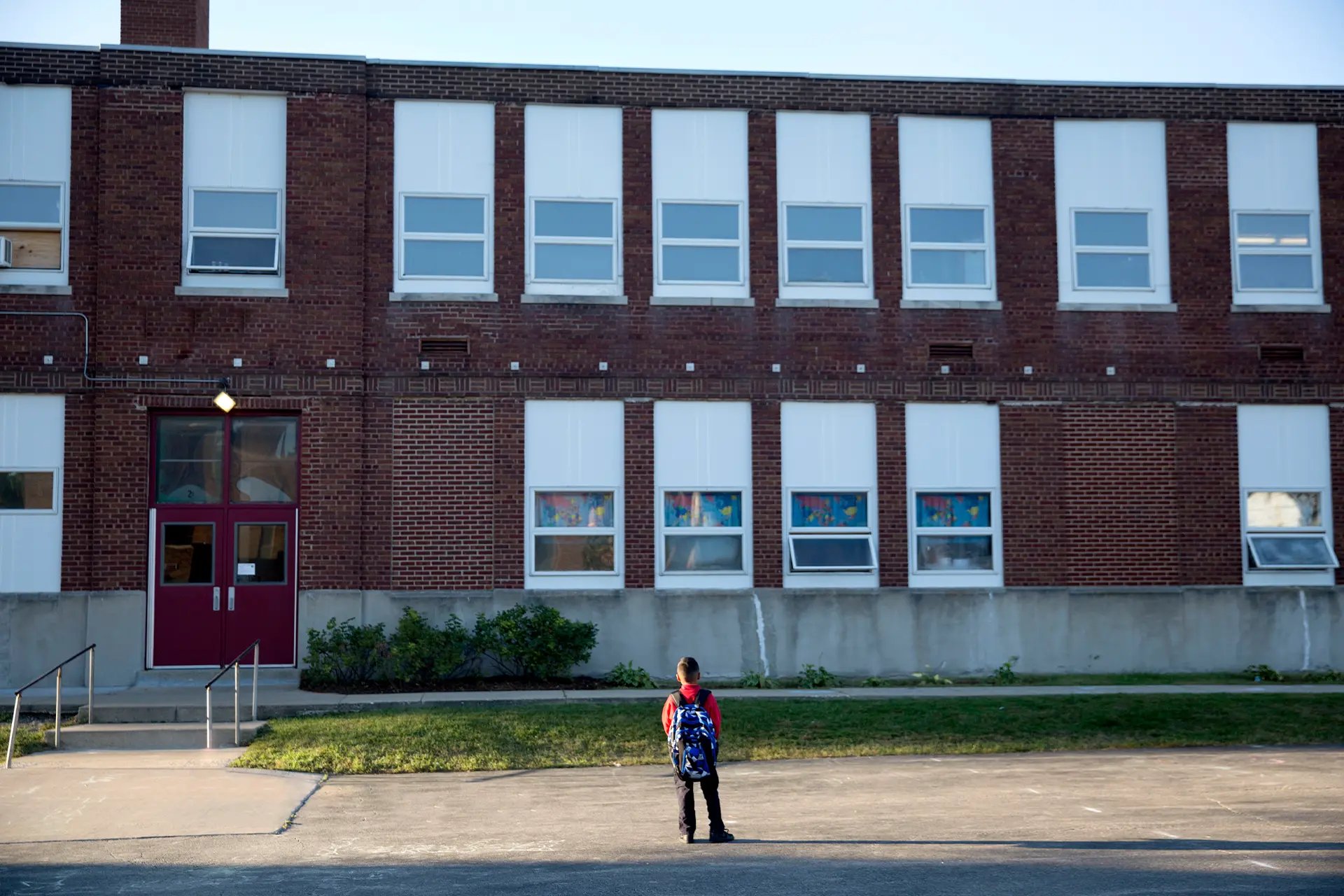 A schoolboy standing outside a large brick school building