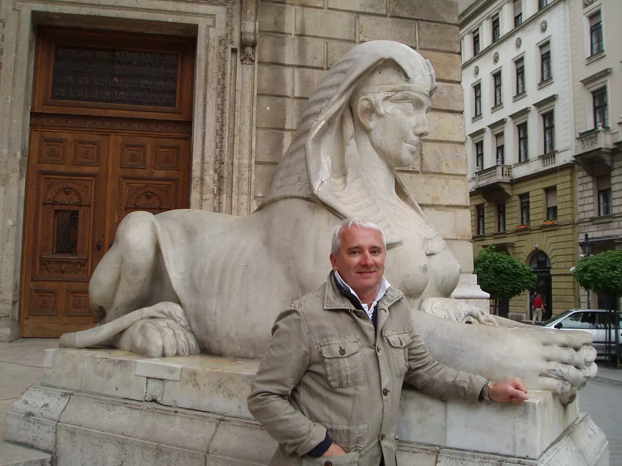 White-haired man standing next to medium sized stone sphinx