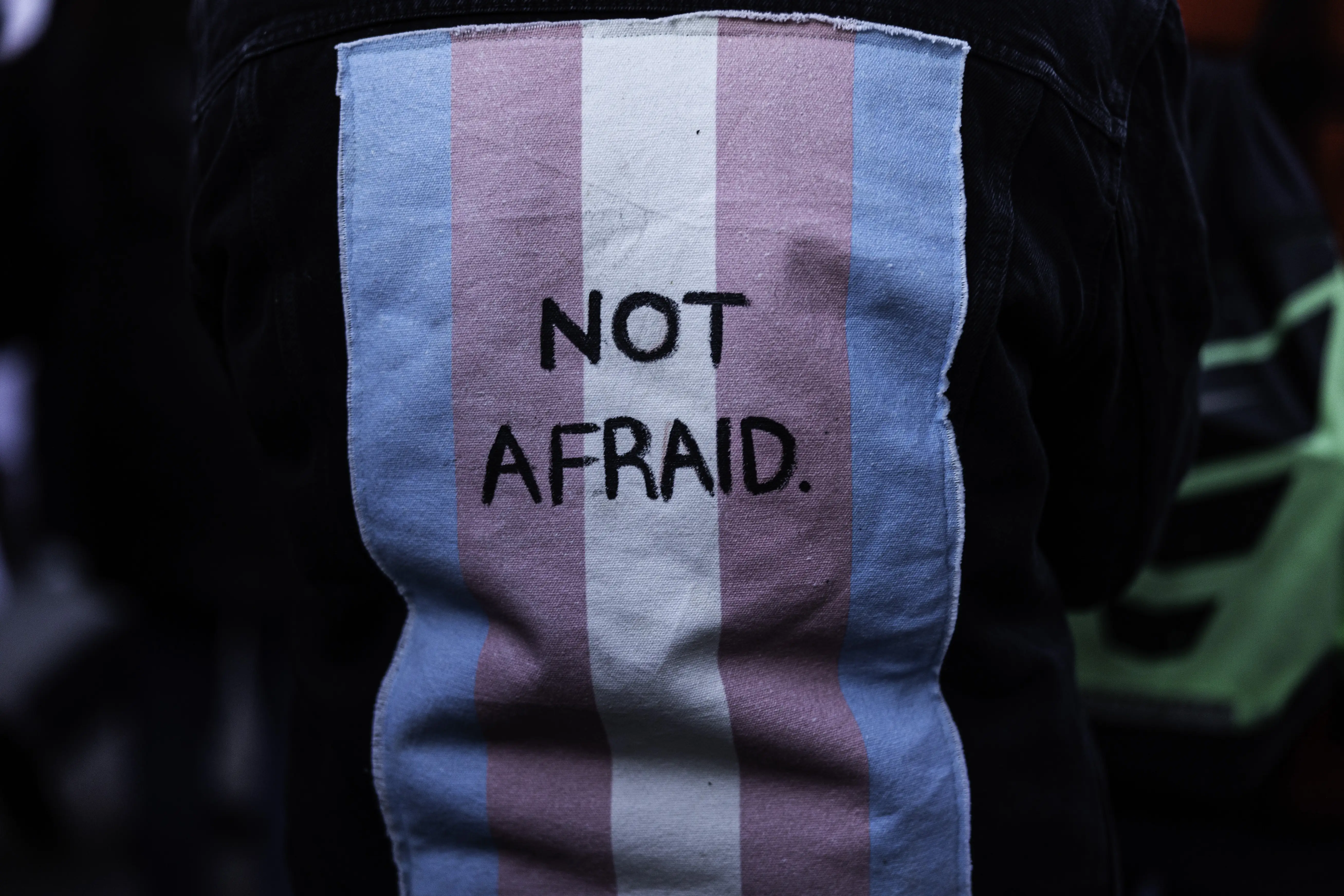 A person wears a vest with a trans flag on the back with the words Not afraid during a memorial honouring trans individuals