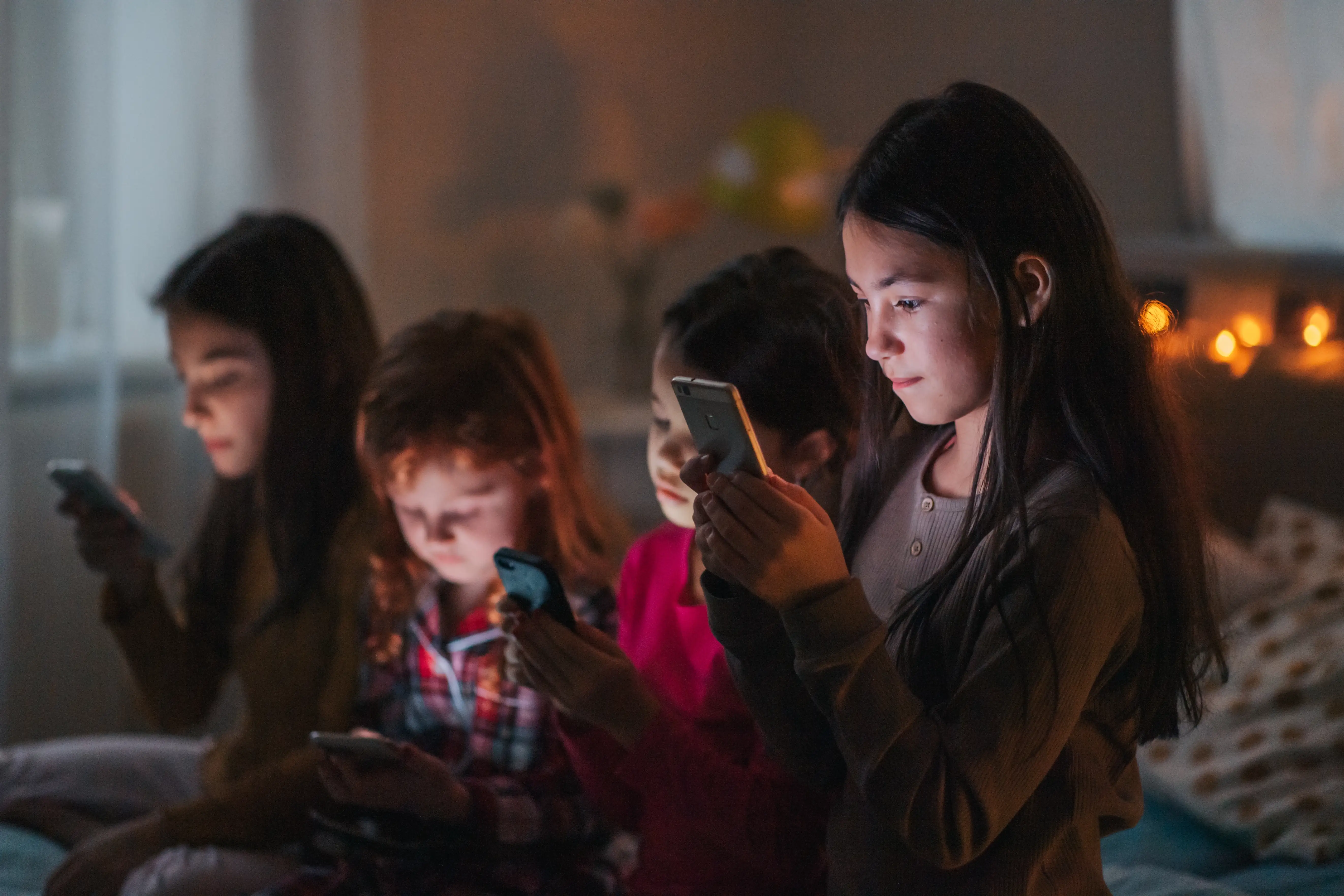 Four children with their faces illuminated by phone screens