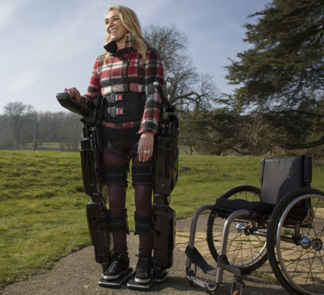 Person wearing an an exoskeleton standing next to a wheelchair.