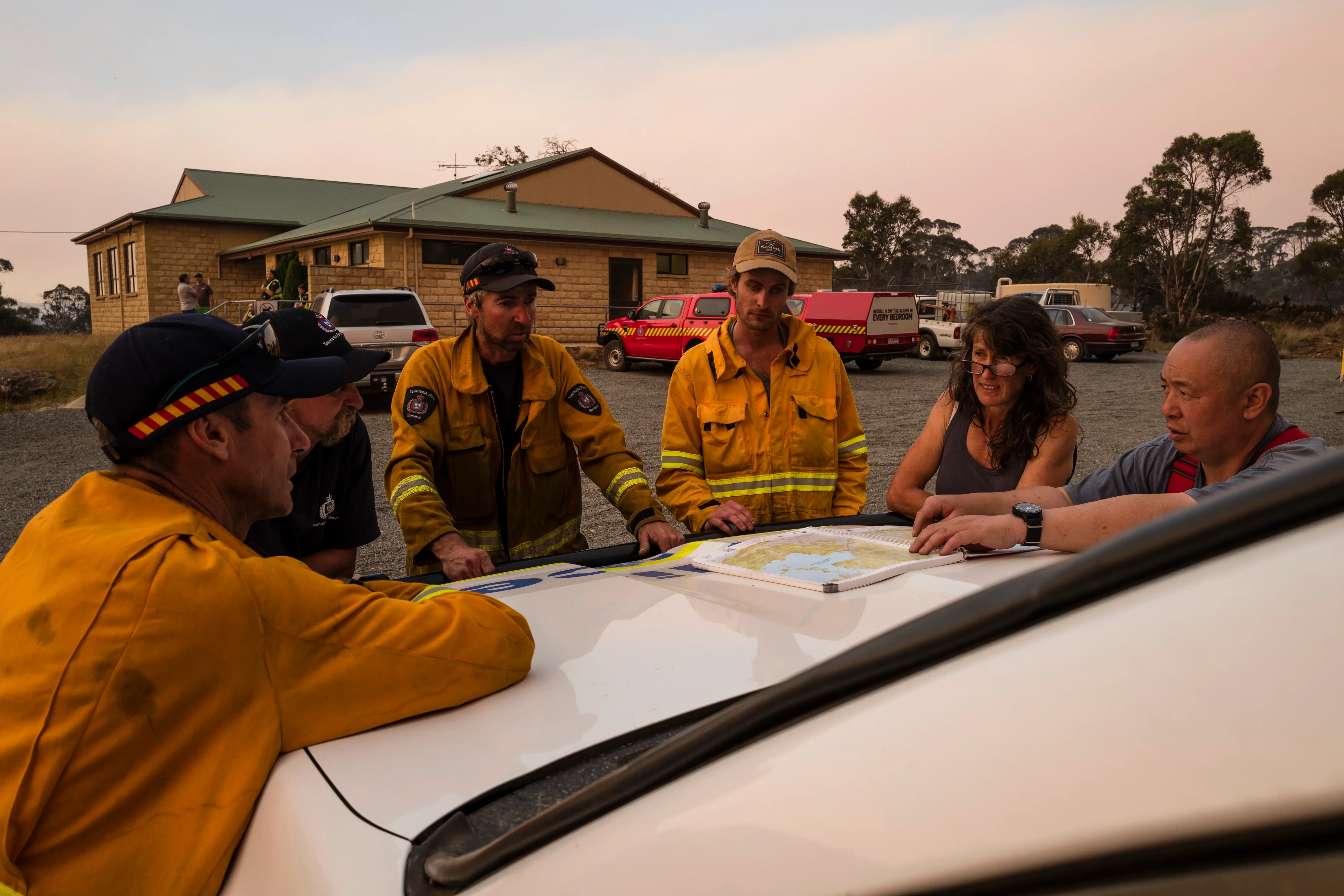 Fire fighters and emergency experts stand around a map placed on the hood of a car as they plan for bushfire